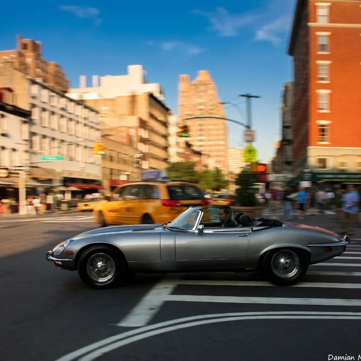 A restored Jaguar E-Type roadster driven through a New York City intersection